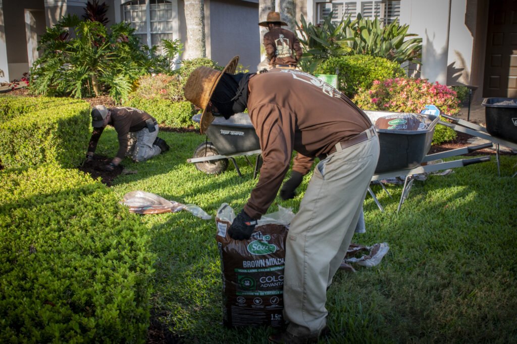 Copperhead professional landscaping crew applying fresh brown mulch to residential flower beds, improving soil moisture retention, weed control, and overall curb appeal in Bexley, FL